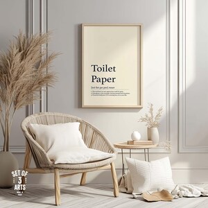Pode incluir: Uma impressão emoldurada com as palavras "Toilet Paper" e sua definição. A impressão está pendurada acima de uma cadeira tecida com uma almofada branca. Um vaso com plantas secas e uma pequena mesa lateral também estão na imagem.