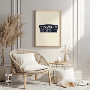 Può includere: Una stampa incorniciata con il testo "5 Guests Flush Wash Spray - The Best" in uno striscione blu navy. La stampa è appesa sopra una sedia intrecciata con un cuscino bianco. Un tavolino e oggetti decorativi completano la scena.