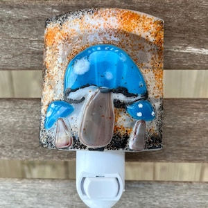 May include: A white night light with a blue, white, and brown mushroom design. The night light has a switch on the bottom.
