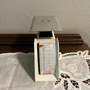 May include: A vintage white and silver program scale with a ribbed top and a measurement dial. The scale measures up to 16 ounces. The text "WEIGHT WATCHERS" is visible on the scale.