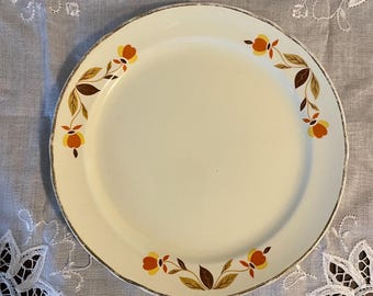 May include: A white ceramic dinner plate with a gold rim and a brown, orange, and yellow floral design.