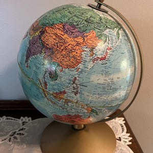 Może przedstawiać: Zabytkowy globus ze złotą podstawą i pierścieniem południkowym. Globus przedstawia szczegółową mapę z krajami w różnych kolorach, w tym pomarańczowym, zielonym i niebieskim. Globus jest przedmiotem dekoracyjnym.