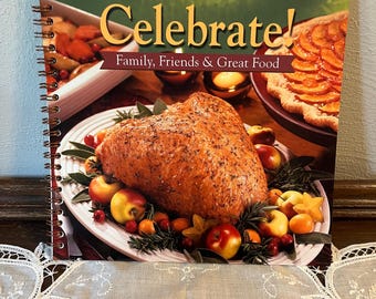 May include: The Pampered Chef cookbook titled "Celebrate! Family, Friends & Great Food" features a roasted turkey on a white platter surrounded by apples, cranberries, and starfruit.