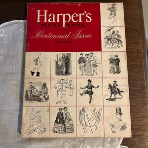 May include: A vintage Harper's Magazine Centennial Issue from 1850-1950. The cover is red with white text and illustrations. The magazine is resting on a white lace doily and a wooden surface.