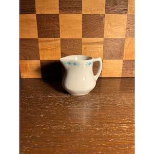 May include: A white ceramic mug with a black handle and the text "But First, Coffee" in a bold, black font. The mug is set against a blurred background, suggesting a cozy setting.