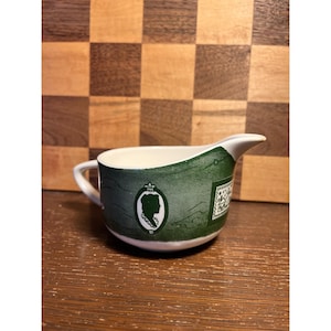 Jarra para crema de cerámica verde con decoración transferida, de la marca Curiosity Shop, con cierta decoloración.