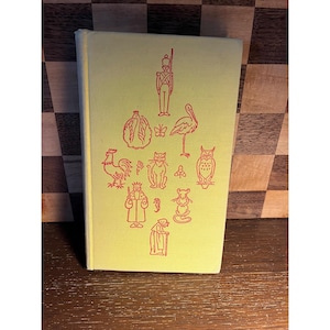 May include: A vintage book with a light yellow cover featuring red illustrations of various animals and figures, including a soldier, rooster, cat, owl, and king. The book is closed and appears to be in good condition.