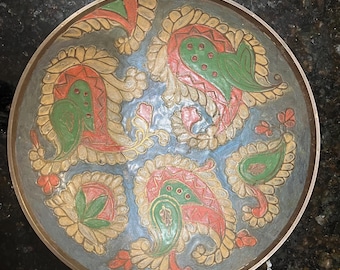 May include: Round metal decorative plate with a dark teal background and colorful paisley designs. The paisley designs are in red, green, and gold. The plate has a gold rim.