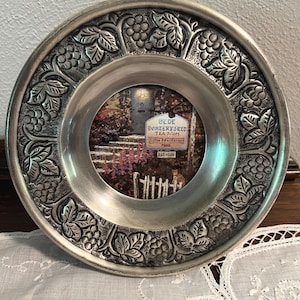 May include: A round, silver-toned picture frame with an embossed grape and leaf design around the edge. The frame holds a small, colorful image of a tea room. The text "OLDE PORTERFIELD TEA ROOM" is visible in the image.