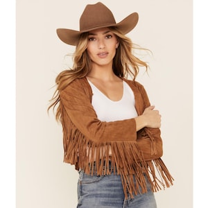 May include: A brown suede jacket with fringe detailing. The jacket has a cropped length and long sleeves. The model is wearing a white tank top and blue jeans.