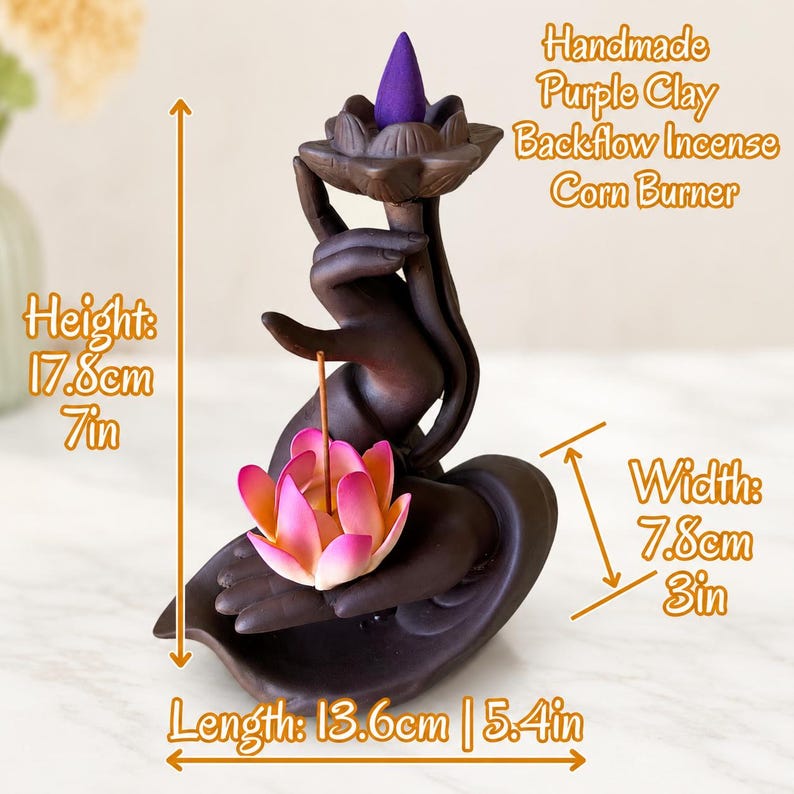 May include: A dark brown purple clay backflow incense burner shaped like a hand holding a lotus flower. It features a purple incense cone on top and a pink lotus flower in the palm. Dimensions are 17.8cm height, 7.8cm width, and 13.6cm length.