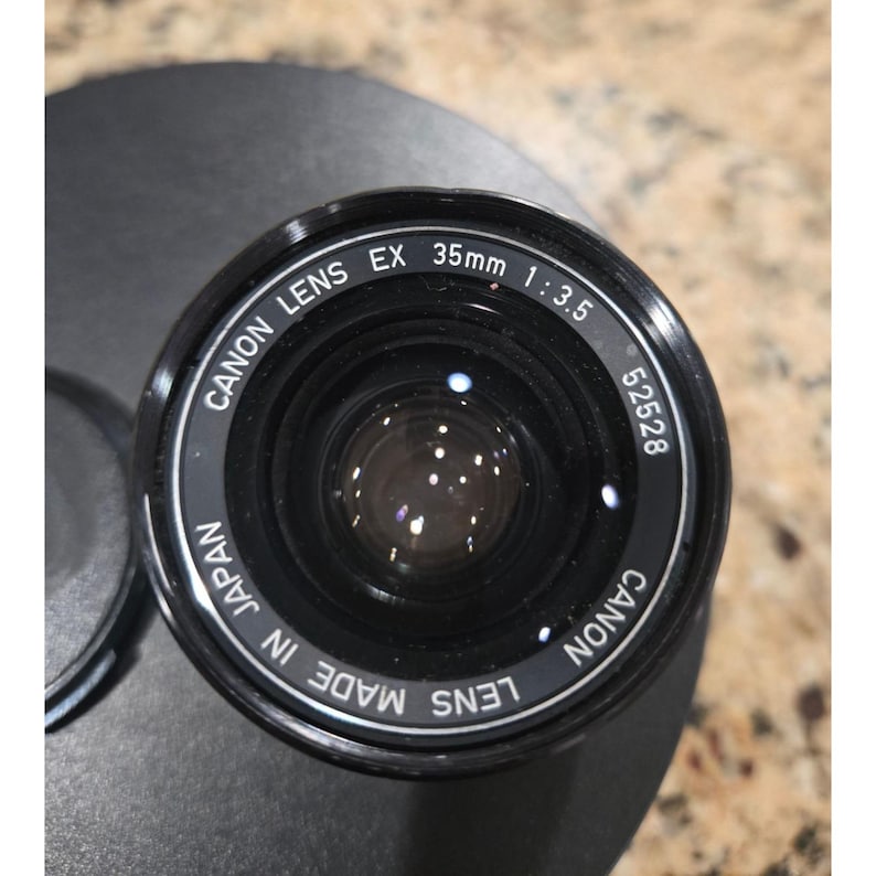 May include: A white ceramic mug with a black handle and the text "But First, Coffee" in a bold, black font. The mug is set against a blurred background, suggesting a cozy setting. The mug appears to be approximately 4 inches tall.