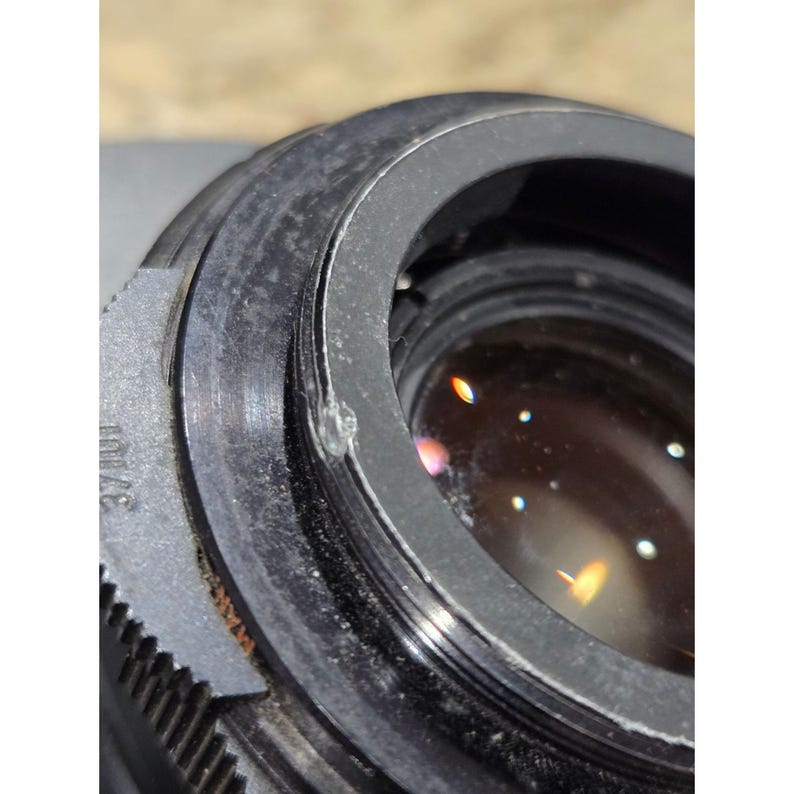 以下が含まれることがあります： シルバーのリングとテクスチャード加工された外側のリングが付いた、黒いカメラレンズのクローズアップ。 レンズには、光の反射がある透明なガラス要素があります。 レンズの側面には「37/101」の数字がエッチングされています。