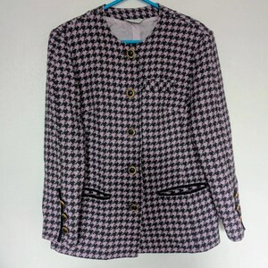 May include: A houndstooth patterned blazer in black and lavender, featuring gold buttons and black trim. The jacket has a round neckline and is hanging on a blue hanger. The blazer has two front pockets.