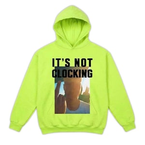 May include: Bright green hoodie with the text "IT'S NOT CLOCKING" in black. The hoodie has a graphic of a person giving the middle finger. It features a hood and long sleeves.