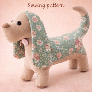 May include: A plush dog toy with a floral pattern on its ears and back. The dog is beige with a light pink collar and a button. The text "Sewing pattern" is at the top of the image.