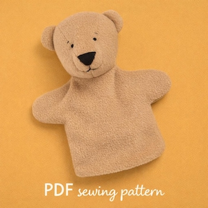 以下が含まれることがあります： 黒い鼻と縫い付けられた目の茶色のテディベアの手の人形。人形は柔らかく、質感のある生地で作られており、シンプルなデザインです。「PDF sewing pattern」というテキストが下にあります。