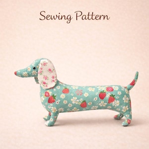 Może przedstawiać: Pluszowy jamnik z jasnoniebieskim korpusem pokrytym wzorem truskawek i białych kwiatów. Uszy psa są wzorzyste z różowymi kwiatami. Nos jest czerwony, a ogon ma wzór truskawki. Tekst "Sewing Pattern" znajduje się nad psem.