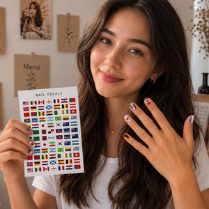 Op de afbeelding: Een rechthoekig vel met nagelstickers met een raster van diverse internationale vlaggen in levendige kleuren, met de tekst NAIL DECALS bovenaan gedrukt. Het vel toont rijen kleine, zelfklevende vlagontwerpen voor toepassing op vingernagels.