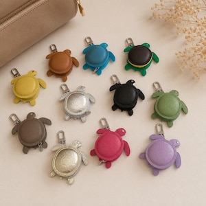 May include: A collection of twelve turtle-shaped coin pouches in various colours including brown, blue, black, yellow, silver, green, grey, pink, and purple. Each pouch features a metal zip closure and a silver-toned metal lobster clasp.