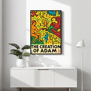 以下が含まれることがあります： 「アダムの創造」のカラフルなイラストが描かれた額入りのアートプリント。 2人の人物が手を伸ばし、鮮やかな形や模様に囲まれています。 タイトル「THE CREATION OF ADAM」が下部に太字で表示されています。