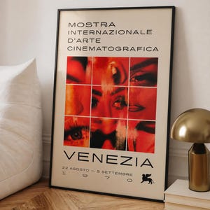 May include: A framed poster for the 1997 Venice International Film Festival, featuring the text MOSTRA INTERNAZIONALE D'ARTE CINEMATOGRAFICA VENEZIA 22 AGOSTO - 5 SETTEMBRE 1970. The center displays a grid of nine red-toned close-up facial images.