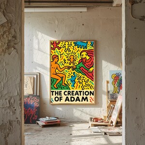 以下が含まれることがあります： アダムの創造の鮮やかなイラストが描かれた額入りのポスター。このアートワークは、黒いテキストが書かれた黄色の背景に、腕を伸ばした2つの人物を描いています。ポスターは、素朴でインダストリアルな環境に展示されています。
