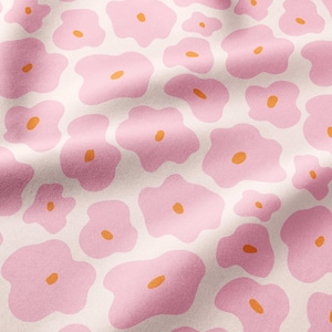 May include: A textile fabric featuring a repeating pattern of irregular, soft pink flower shapes on a light cream background. Each pink flower contains a small, centered, oval-shaped orange dot. The fabric surface shows subtle folds and shadows.