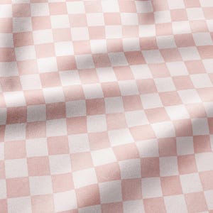 May include: A textile fabric featuring a repeating checkered pattern in soft pastel pink and white. The material displays gentle folds and soft shadows, highlighting the smooth texture and the consistent square grid design across the surface.