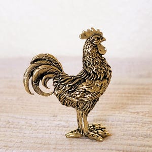 May include: A gold-colored rooster figurine with detailed feathers and a standing pose.