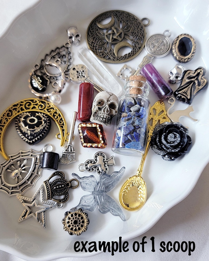 May include: A white bowl filled with a variety of charms, beads, and other small decorative items. The items include a skull, a crescent moon, a butterfly, a spider, a crown, a spoon, a bottle of blue stones, and a black rose.