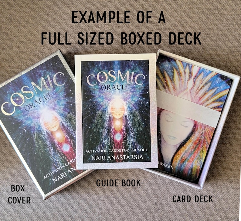 Op de afbeelding: Een full-size boxed deck van Cosmic Oracle kaarten. De doos en het gidsboek tonen de titel en illustratie van een vrouw met een gloeiende aura. Het kaartspel is zichtbaar in de doos, met een witte band.