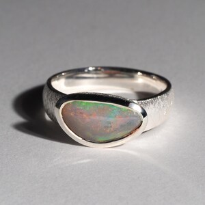 May include: A silver ring with a textured band and a bezel setting featuring a green and white opal.