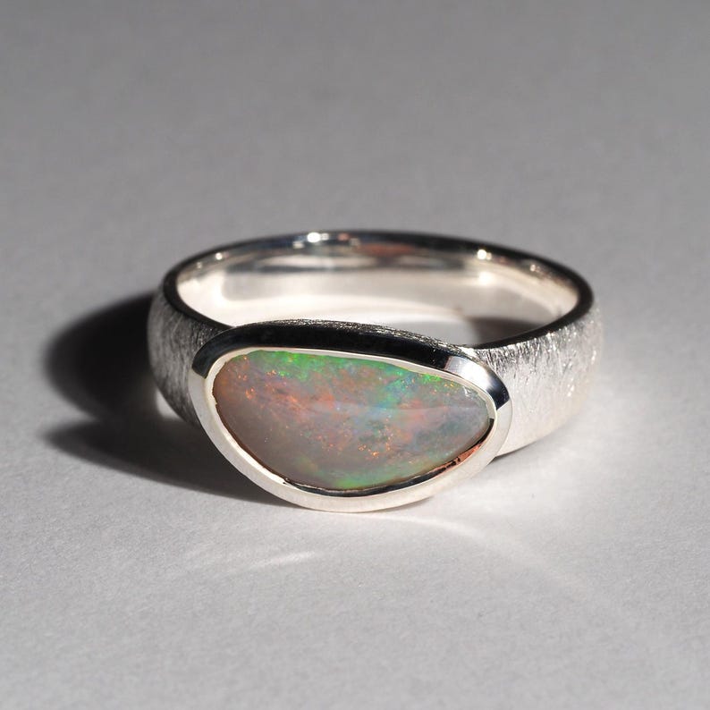 May include: A silver ring with a textured band and a bezel setting featuring a green and white opal.