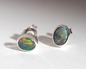 Puede incluir: Un par de pendientes de plata con ópalos ovalados e iridiscentes. Los ópalos muestran una vibrante gama de colores, incluyendo verde, amarillo y naranja, engastados en un bisel de plata pulida. Una joya.