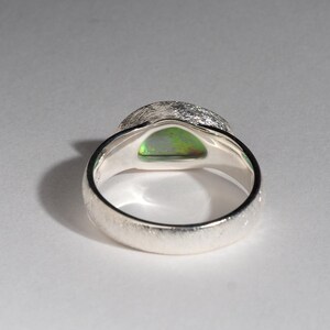 May include: A silver ring with a textured band and a green opal gemstone set in the center.