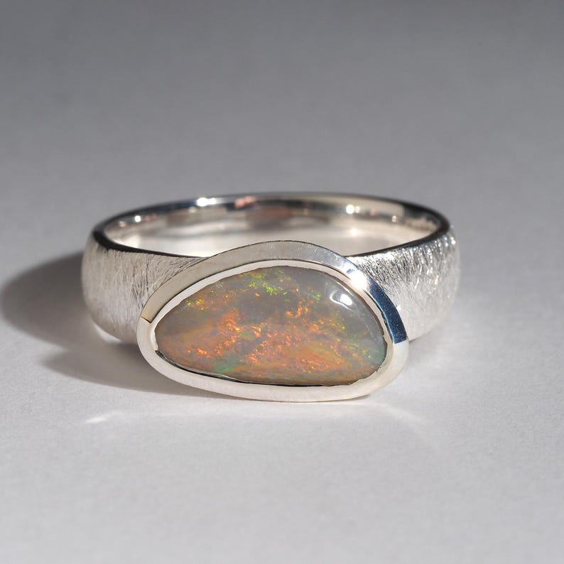 May include: A silver ring with a textured band and a pear-shaped opal gemstone set in a bezel setting.