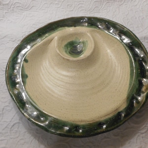 Puede incluir: Un plato de servir de cerámica con un borde verde y una sección central elevada. El plato está salpicado de esmalte marrón y blanco.