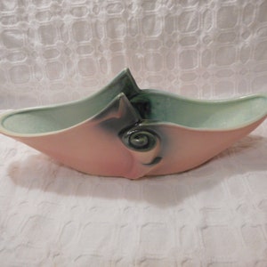 Può includere: Un vaso da fiori in ceramica rosa e verde con un design astratto unico. Il vaso ha la forma di una barca con una parte superiore curva e aperta.