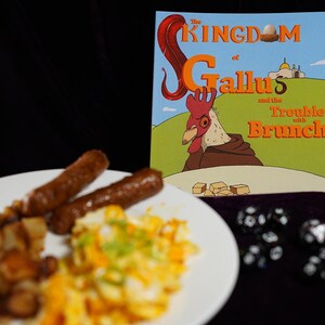 Può includere: Un piatto di cibo per la colazione con uova strapazzate, salsicce e patate fritte. Un libro intitolato "The Kingdom of Gallus and the Trouble with Brunch" è sullo sfondo.