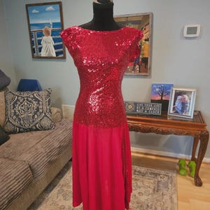 May include: A red sequined dress displayed on a black mannequin. The top of the dress is covered in red sequins, while the skirt is a flowing red fabric. The dress is designed for a formal occasion.