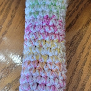 May include: A colorful crocheted pot holder with stripes of green, yellow, pink, and blue.