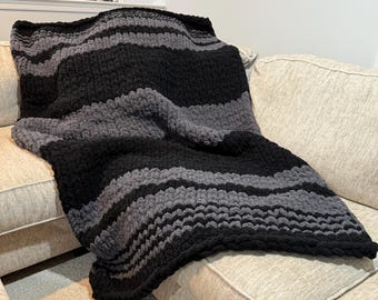 May include: A black and gray striped crocheted throw blanket draped over a couch.