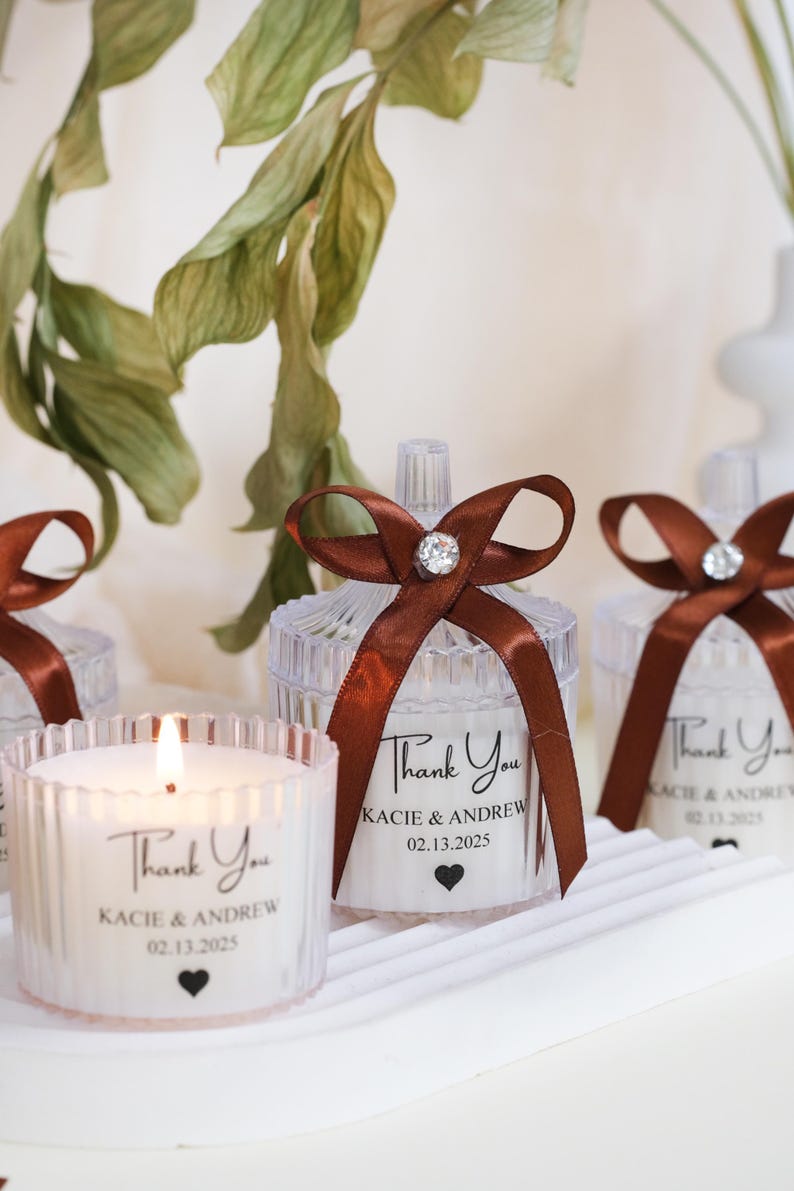 May include: Clear glass candle jars with brown ribbon bows and personalized labels that say "Thank You Kacie & Andrew 02.13.2025".