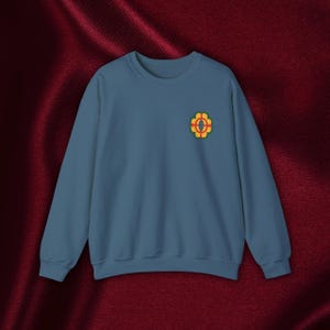 Könnte beinhalten: Ein blaues Sweatshirt mit einer gestickten gelben, roten und grünen Blume auf der linken Brust.