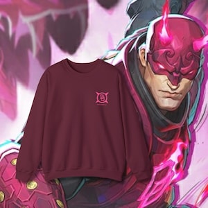 May include: A maroon crewneck sweatshirt with a small pink logo on the chest. The logo is a stylized design with the text "The Daredevil". The background features a comic book style illustration of a character in a mask.