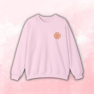 Könnte beinhalten: Ein rosa Sweatshirt mit einem rosa und goldenen Blumendesign auf der linken Brust.