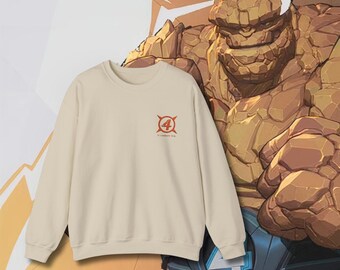 May include: A beige sweatshirt with a graphic of a red circle with a white number four inside and four white lines radiating out from the circle. The text "Fantastic Four" is printed in small white letters below the circle. The sweatshirt is shown against a background of a cartoon image of the Thing from the Fantastic Four.