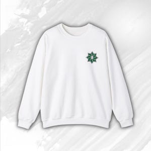 Könnte beinhalten: Weißer Pullover mit einem grünen sternförmigen Design auf der Vorderseite.