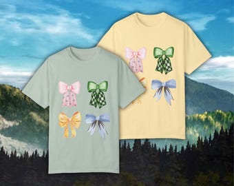 May include: Two t-shirts with different colored bows printed on them. The shirt on the left is light green with yellow, pink, blue, and green bows. The shirt on the right is yellow with pink, green, and blue bows.